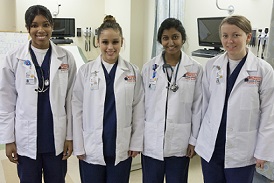 four nursing students in blue scrubs and white lab coats